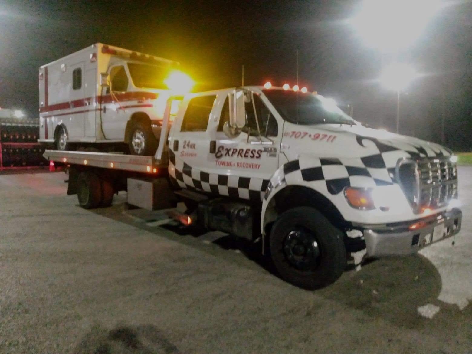 Express Towing and Recovery truck transporting an ambulance at night