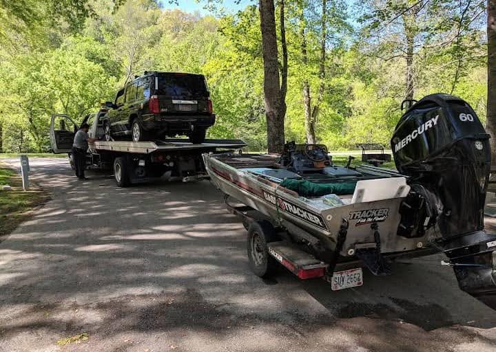 Flatbed tow truck transporting a vehicle near a boat trailer